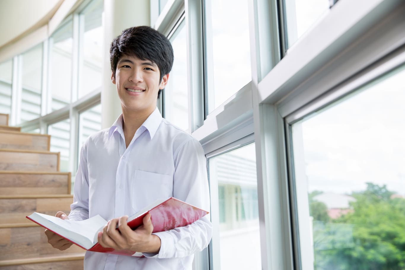 Happy Asian male student holding books at the library